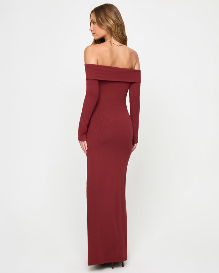 Back view of a model wearing the LSPACE Carrie Dress in sangria, showing the off-the-shoulder folded neckline band, long sleeves, and body-hugging maxi silhouette in ribbed sangria knit fabric.