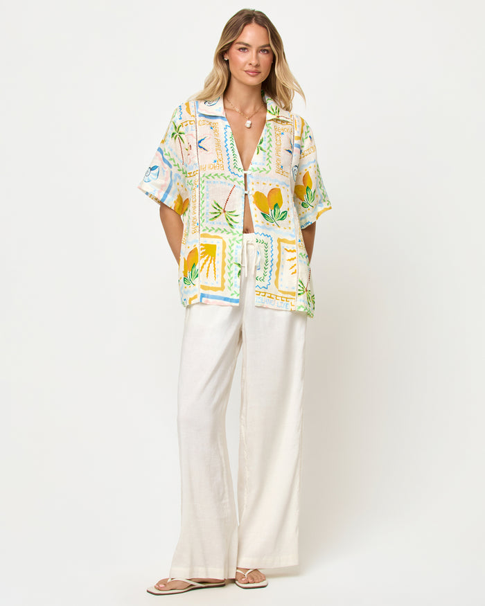 LSPACE La Mer shirt in Wish You Were Here print, front view on model styled with wide-leg pants.