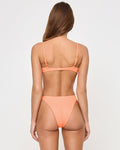 Back view of a model wearing the LSPACE Leilani Bikini Bottom in Fresh Squeezed against a studio background, a peach-orange cheeky bikini bottom with high-cut legs, paired with a matching Fresh Squeezed Belle Bikini Top.