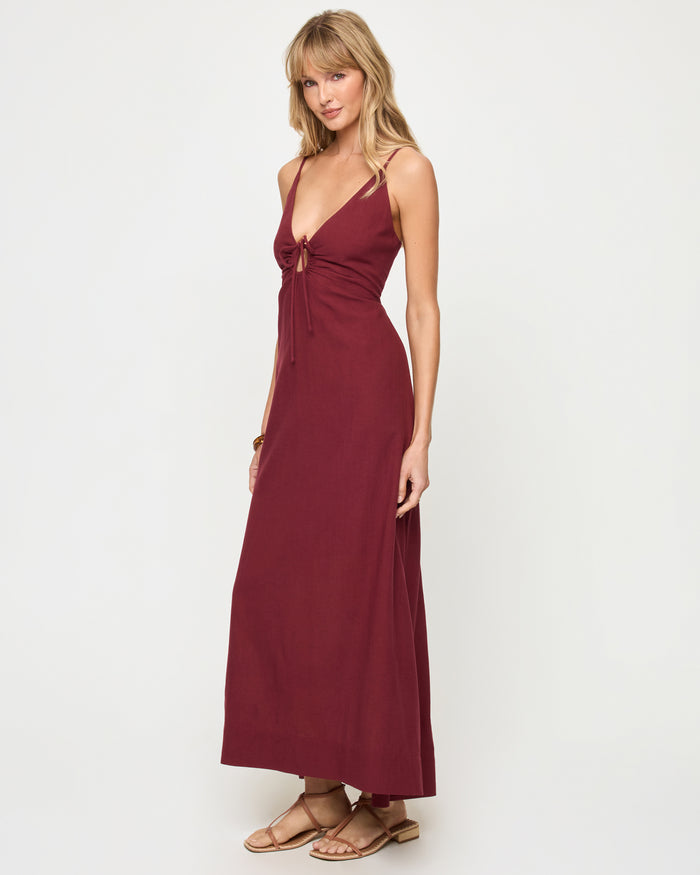 Three-quarter view of a model wearing the LSPACE Mabel Maxi Dress in sangria, featuring thin spaghetti straps, a deep V-neckline with keyhole cutout and tie detail at the bust, and a flowing full-length silhouette.