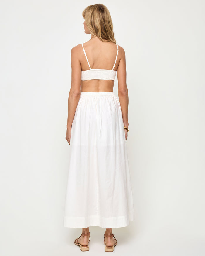 Back view of a model wearing the LSPACE Manon Top in white, featuring thin spaghetti straps with hardware detail and an open back with banded hem.