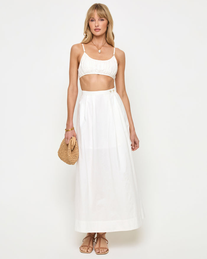 Front view of a model wearing the LSPACE Manon Top in white, featuring thin spaghetti straps, a ruched scoop neckline, and a cropped silhouette, styled with a white maxi skirt.