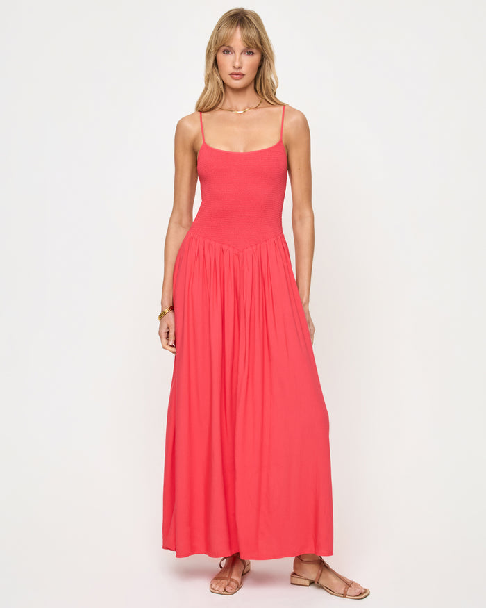 Front view of a model wearing the LSPACE Misha Midi in pout, featuring thin spaghetti straps, a square neckline, a smocked fitted bodice, and a full flowing coral pink skirt.