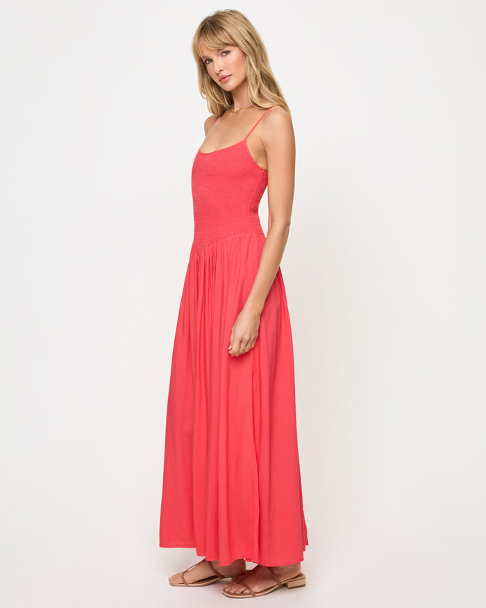 Side view of a model wearing the LSPACE Misha Midi in pout, showing thin spaghetti straps, a smocked bodice, and a full flowing coral pink skirt.