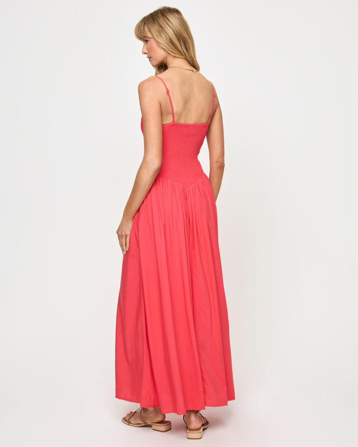 Back view of a model wearing the LSPACE Misha Midi in pout, showing thin spaghetti straps, a smocked open back, and a full flowing coral pink skirt.