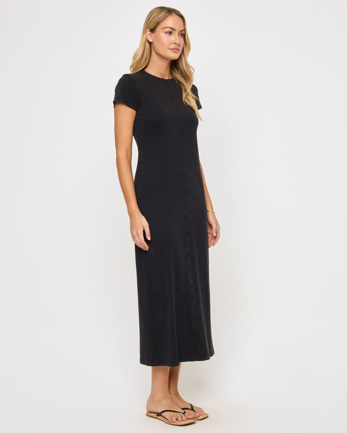 Side view of a model wearing the LSPACE Sloane Dress in black, showing the sleek fitted silhouette of the maxi dress with a crew neckline and short sleeves.
