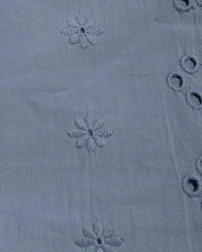 Close-up of a dusty blue fabric with embroidered floral motifs and eyelet embroidery.