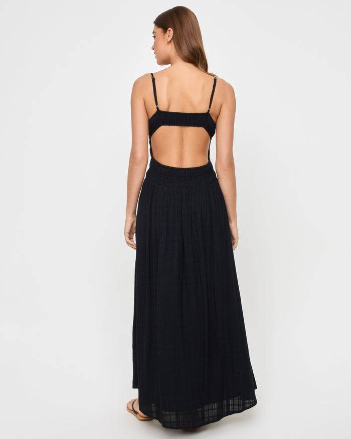 Back view of a model wearing the LSPACE Tala Dress in black, showing the wide open-back cutout between the crop-style bodice and smocked waistband.