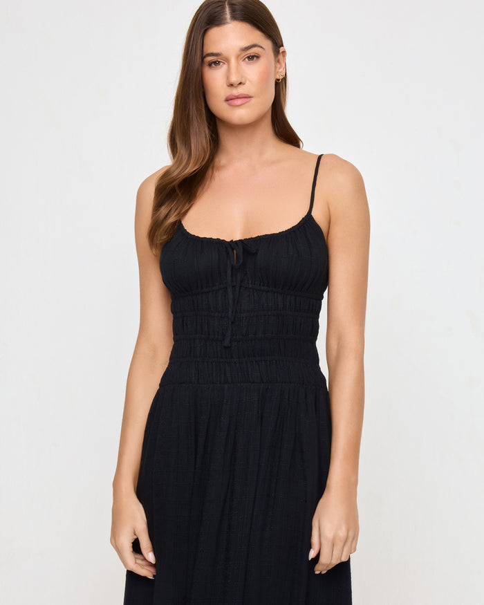 Close-up of a model wearing the LSPACE Tala Dress in black, highlighting the smocked bodice and center front tie detail with a flowing maxi skirt below.